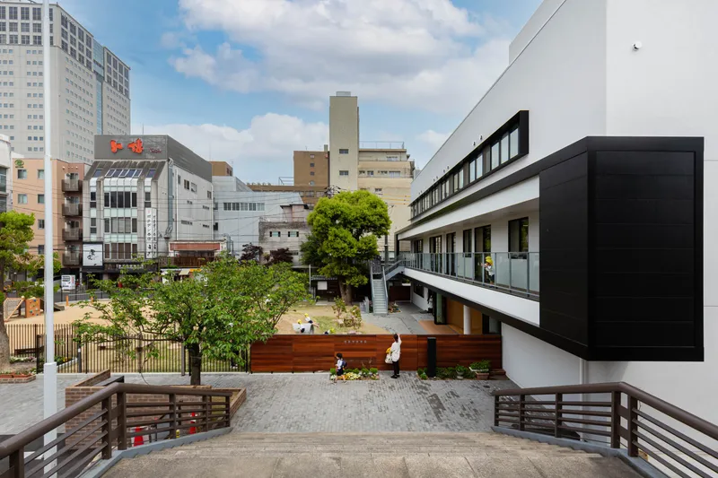 Courtyard view with timber-clad volumes, an elevated walkway and children playing among planted greenery