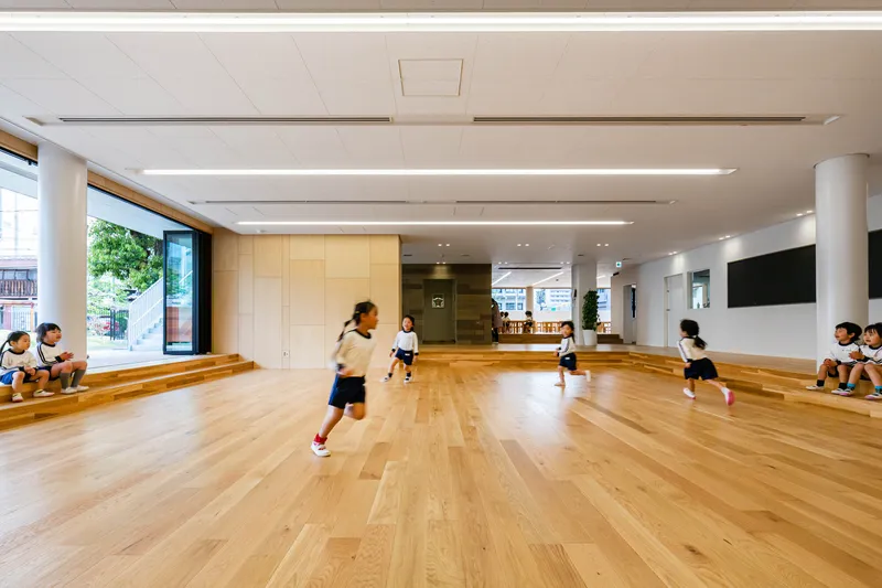 Multi-purpose room with stepped timber seating along one wall and children playing across the floor