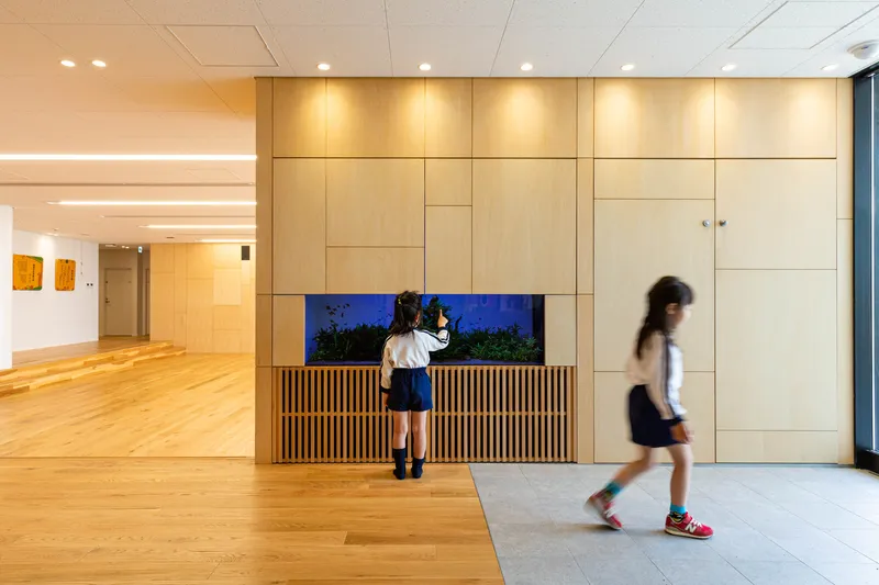 Light timber wall panels with horizontal slat base and narrow aquarium window as children pass