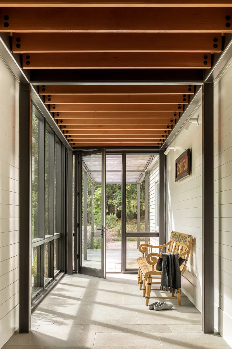 Glazed corridor with horizontal timber ceiling slats and dappled sunlight on tile floor