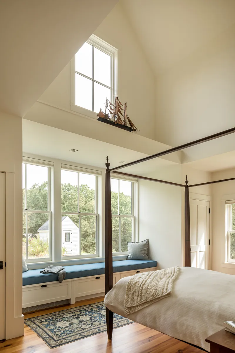 Bedroom with built-in window seat beneath tall windows overlooking trees in summer