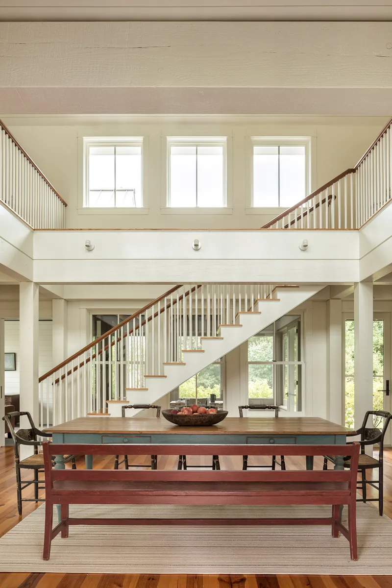 Double-height dining space with open staircase and upper gallery beneath clerestory windows