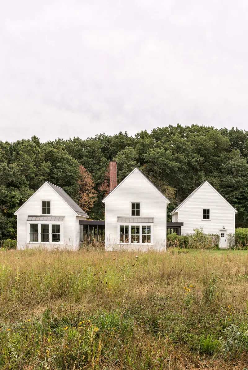 Rear elevation of three connected gabled structures with horizontal siding and brick chimney
