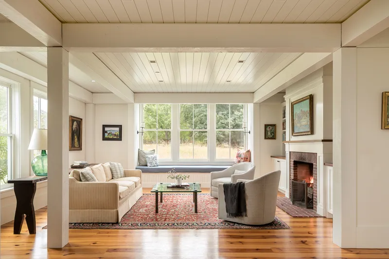 Living room with window seat, fireplace and wood ceiling framed by white columns