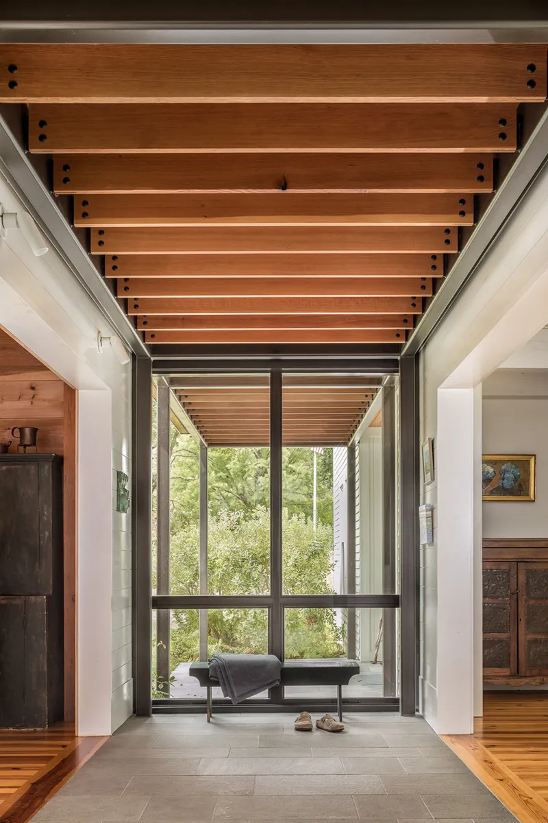 Interior hallway with timber slat ceiling, steel frame glazing, and grey tile floor beneath natural light
