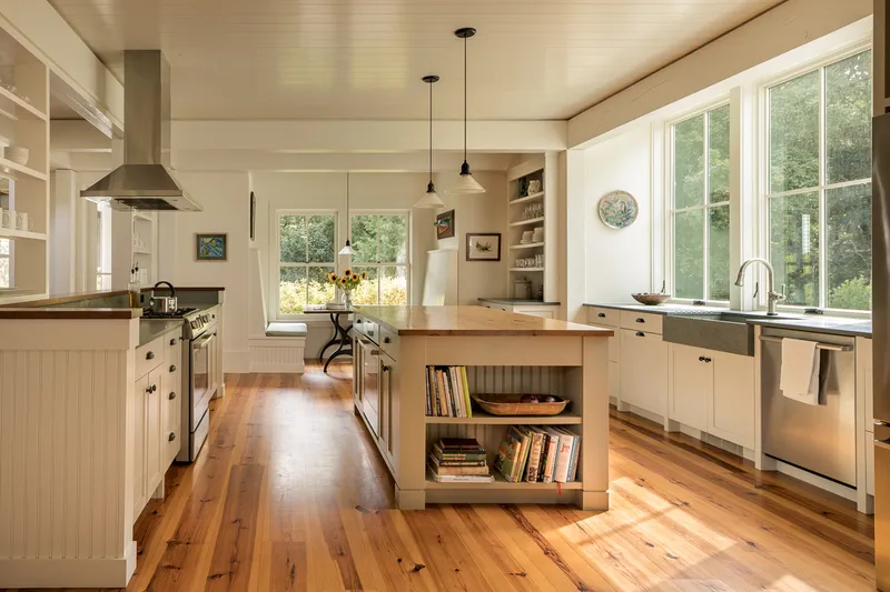 Kitchen with butcher block island, white cabinetry, and wide plank pine flooring beneath pendant lights