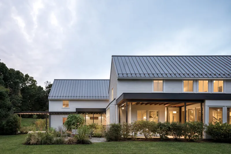 Rear facade with standing seam metal roofs and planted beds along the lawn at twilight