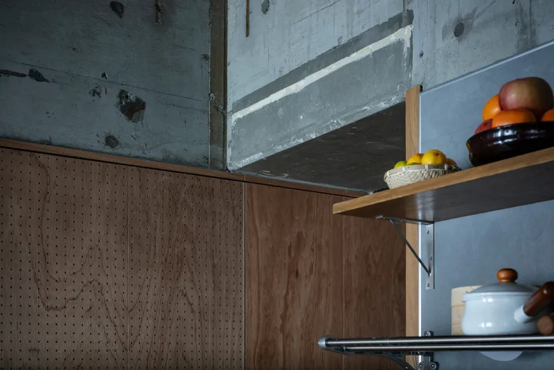 Close-up of perforated wood cabinet edge meeting steel shelves with ceramic containers beneath concrete beam