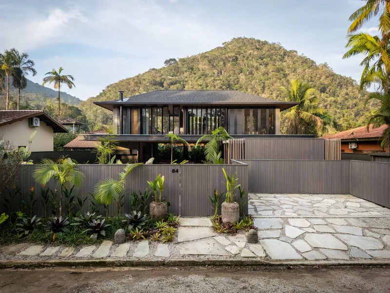 Street view of the two-storey timber facade with horizontal slats against a forested hillside backdrop