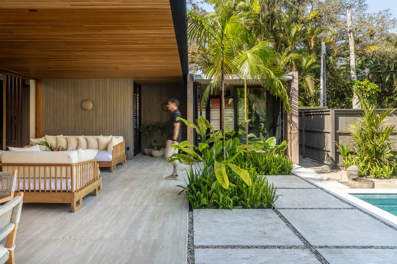 Covered outdoor lounge with timber ceiling and a figure walking past tropical plantings
