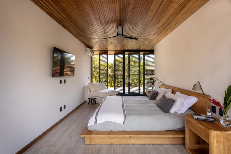 Bedroom interior with timber slat ceiling and louvered doors opening to greenery