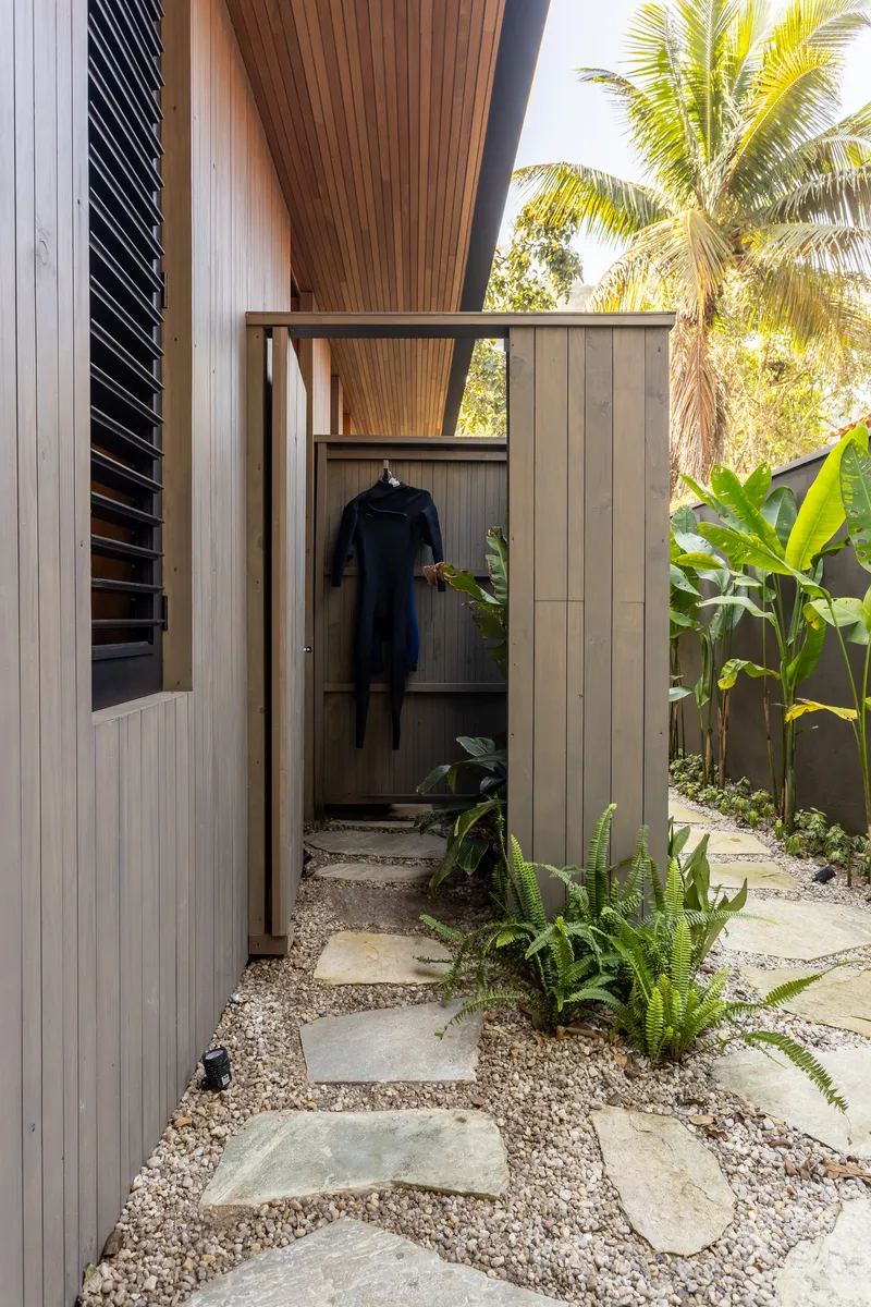 Gravel pathway with stepping stones leading to an outdoor shower with timber-clad walls and a wetsuit
