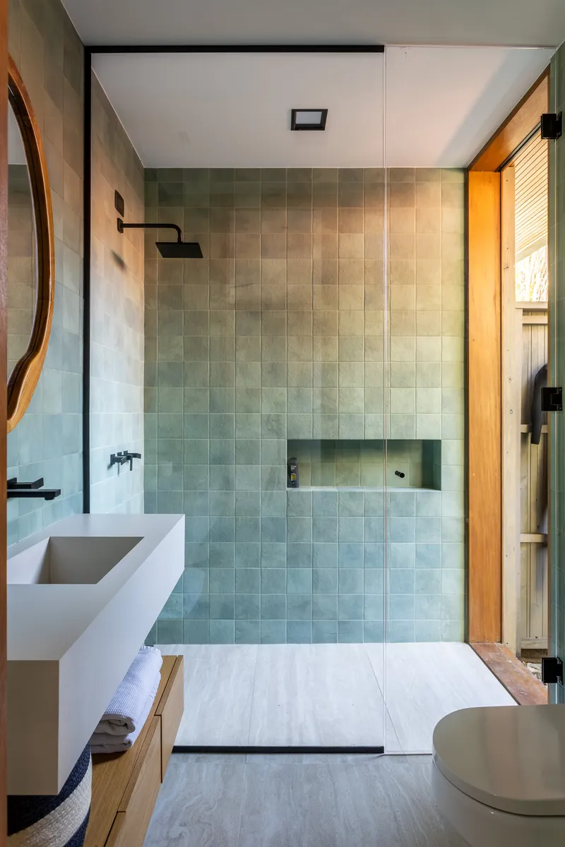 Bathroom with pale green square tiles, recessed niche, black fixtures and a round mirror