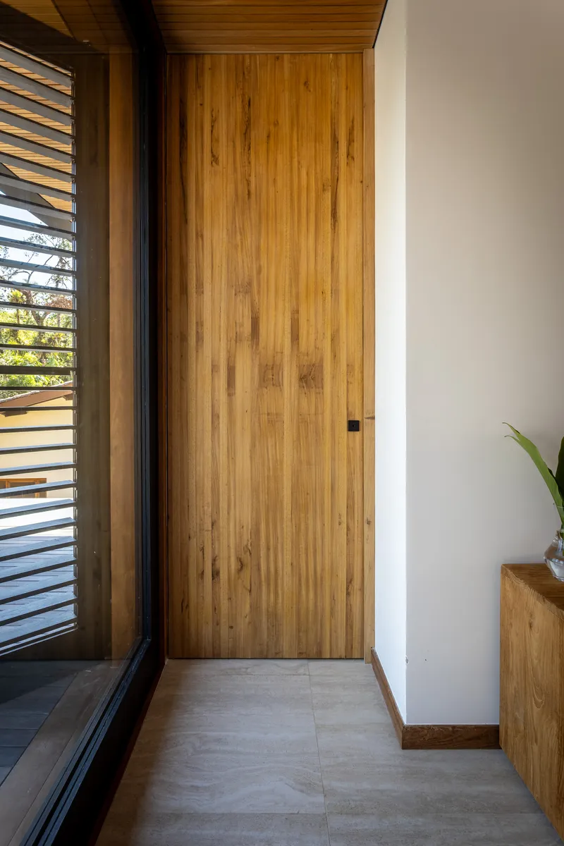 Closed timber pocket door set into a white wall beside a louvered window and console