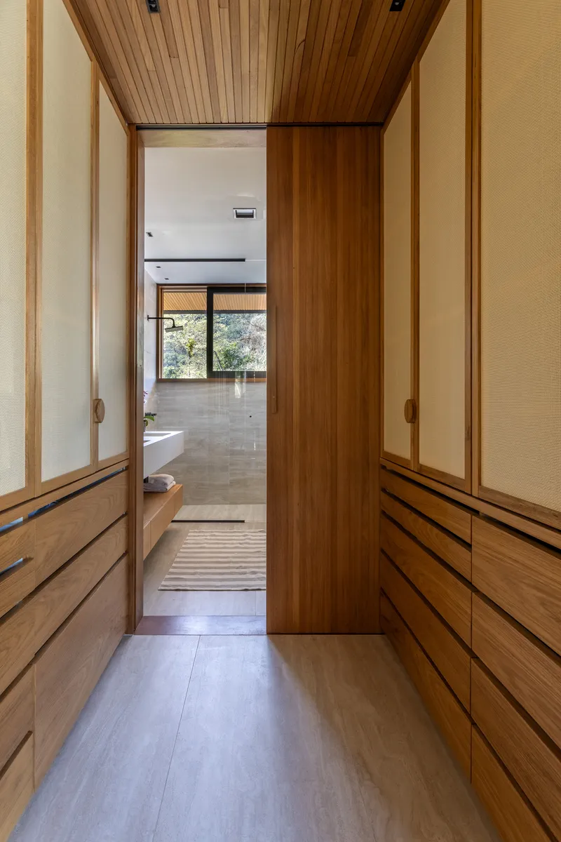 Timber-lined hallway with built-in cabinetry looking through to a room with concrete floors and garden views