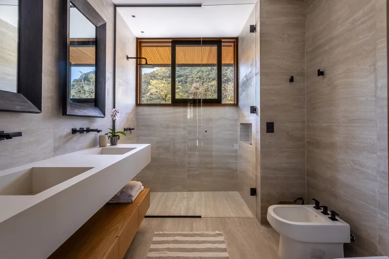 Bathroom with travertine walls, glass shower enclosure, and timber-framed window overlooking hills