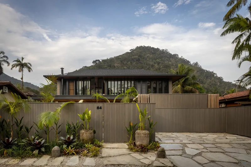 Street facade with vertical timber screening and metal cladding framed by palms and planted beds