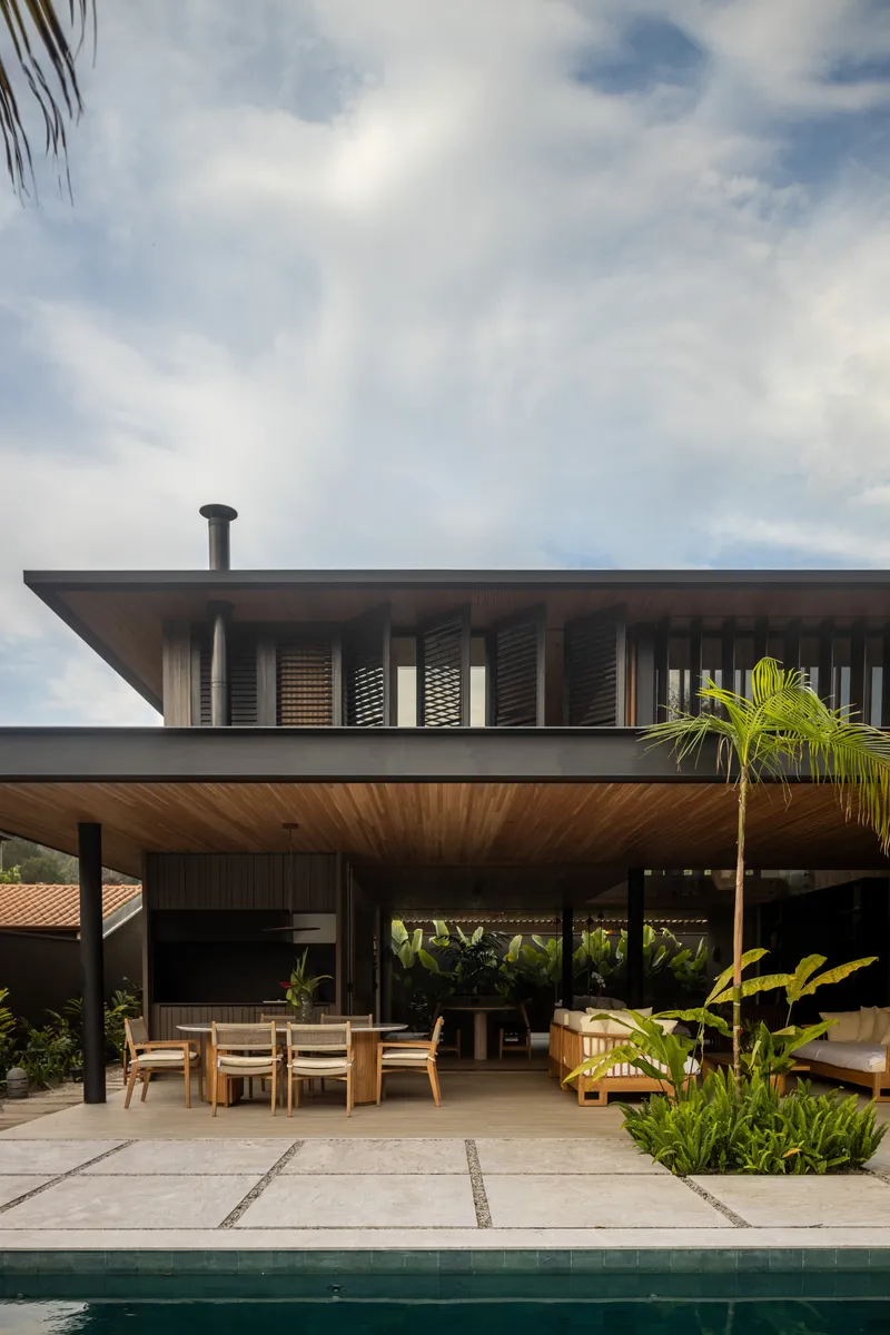Covered poolside terrace with timber soffit, deep overhangs, and louvered upper level under cloudy skies
