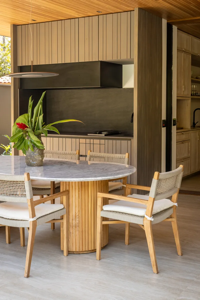 Dining area with marble-topped table beneath timber slat ceiling and integrated black stone kitchen wall