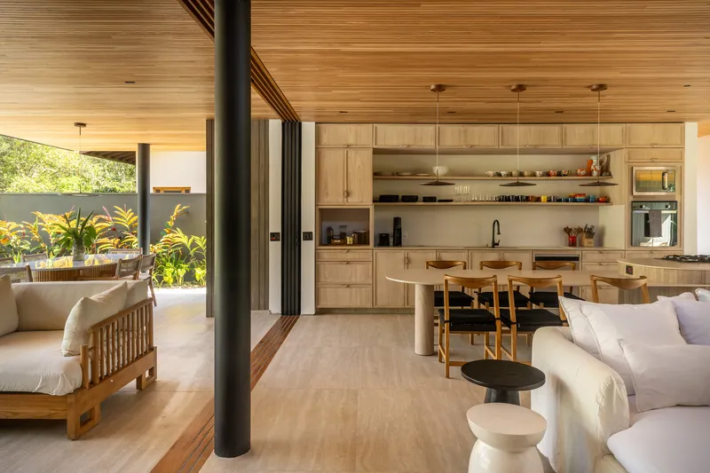 Open-plan living space with timber ceiling, black steel column, and sliding glass doors to planted garden