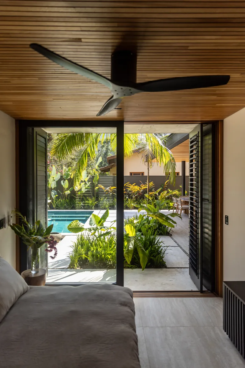 Interior bedroom view through black-framed sliding doors opening to a planted courtyard with pool and palm fronds