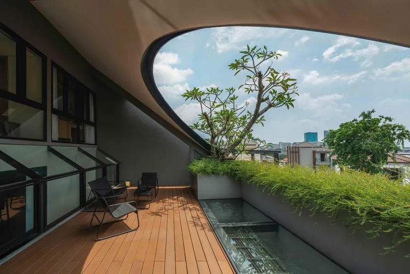 Rooftop terrace with timber decking, planted bed, and frangipani tree under open sky