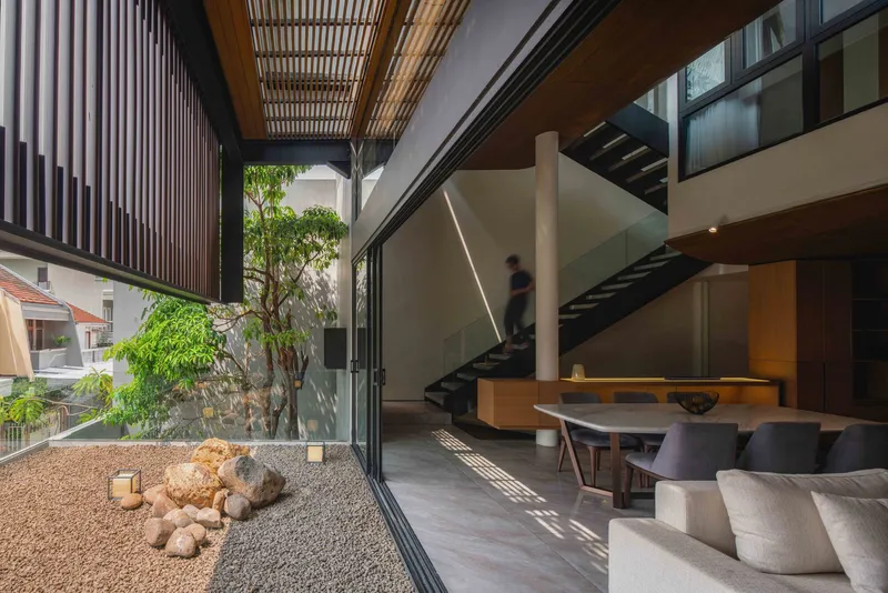 Interior living space opening to courtyard with gravel bed and small tree in dappled sunlight