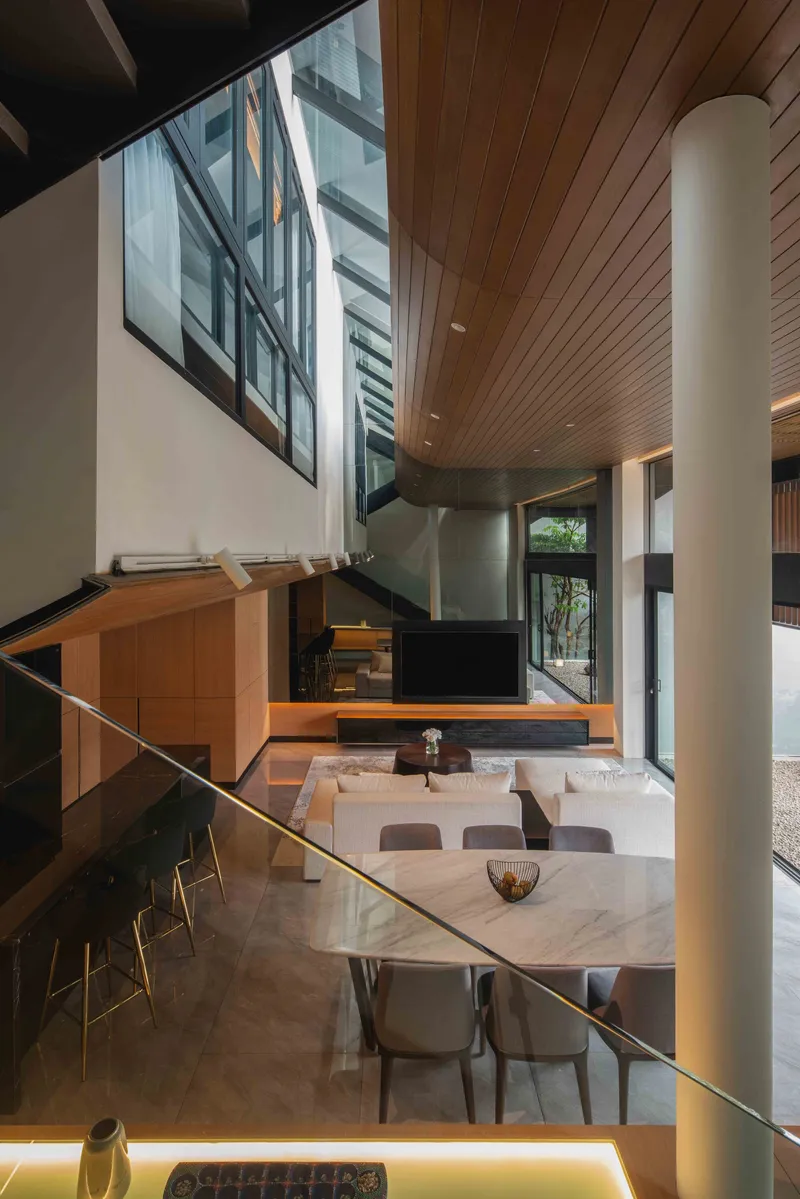 Double-height living area with timber-slat ceiling, cylindrical white column and dining table below clerestory window