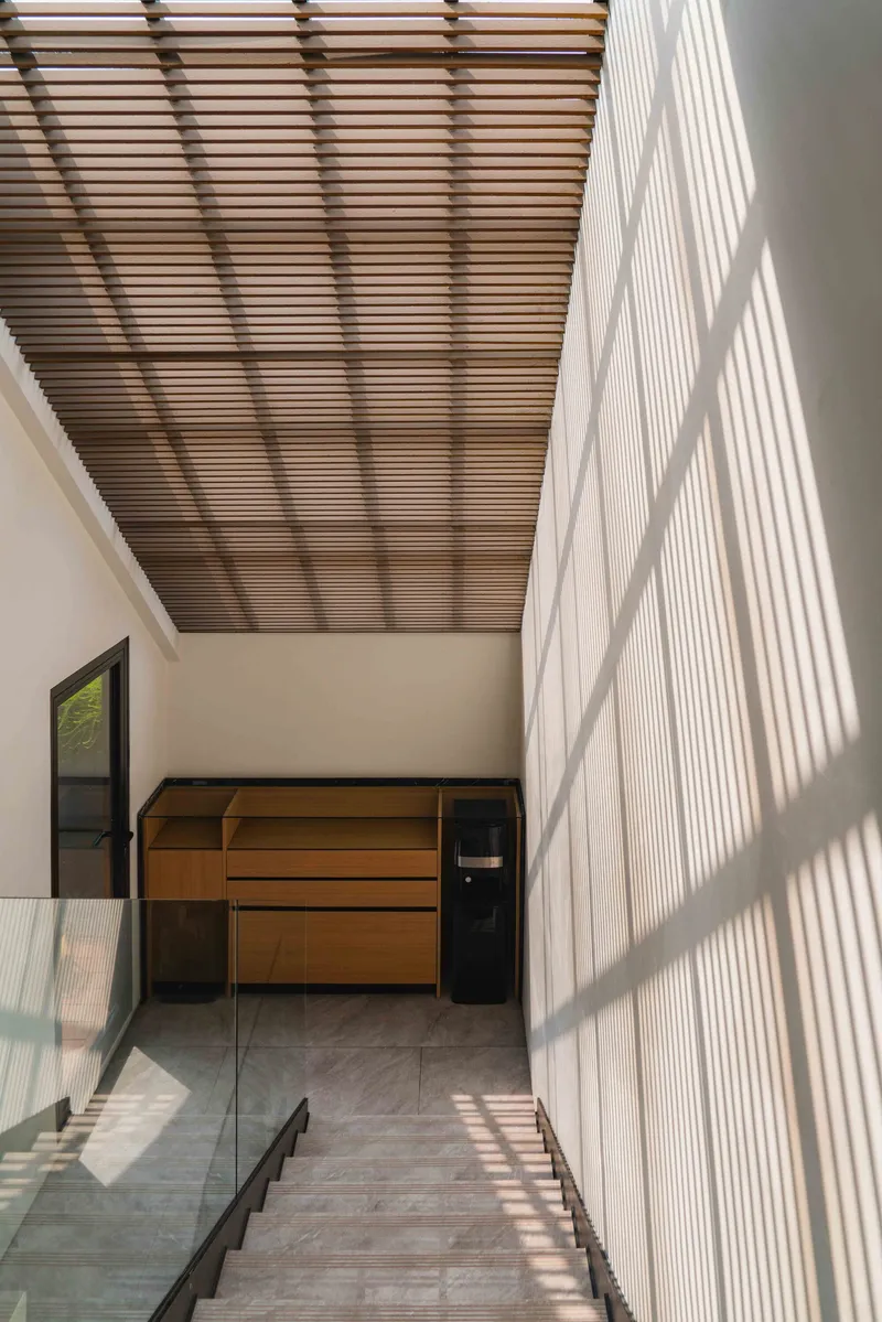 Upper hallway with slatted timber ceiling casting striped shadows across the white wall in bright daylight
