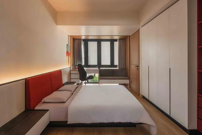 Bedroom with red upholstered headboard wall, white wardrobes and desk beneath the window