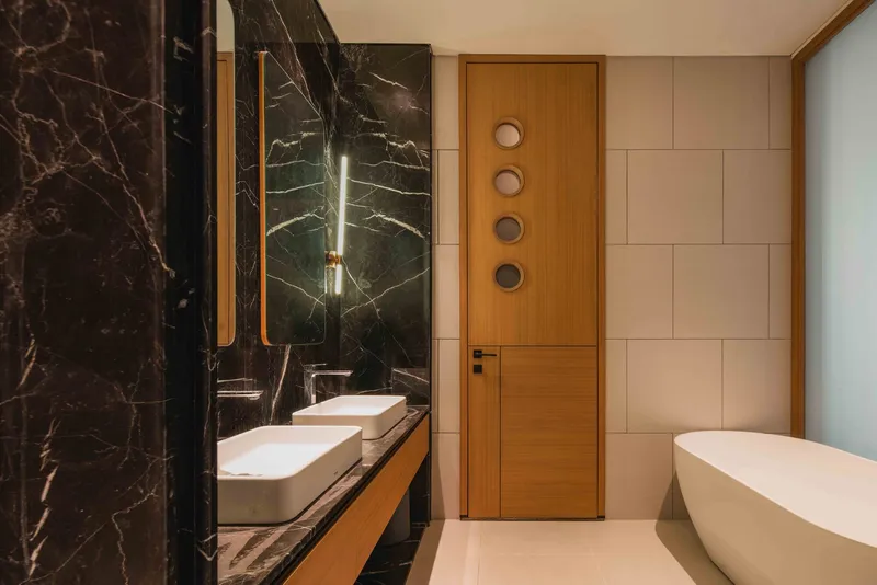 Bathroom with dark veined marble wall, timber door and freestanding white bathtub