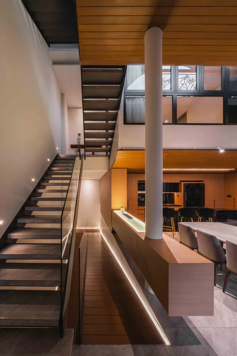 Double-height space with floating timber staircase, white column and LED-lit cabinetry at dusk