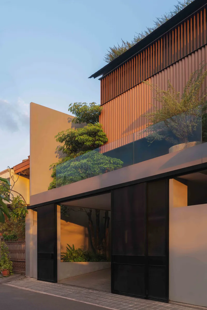Street facade with vertical timber slats and glazed entry beneath planted rooftop at golden hour