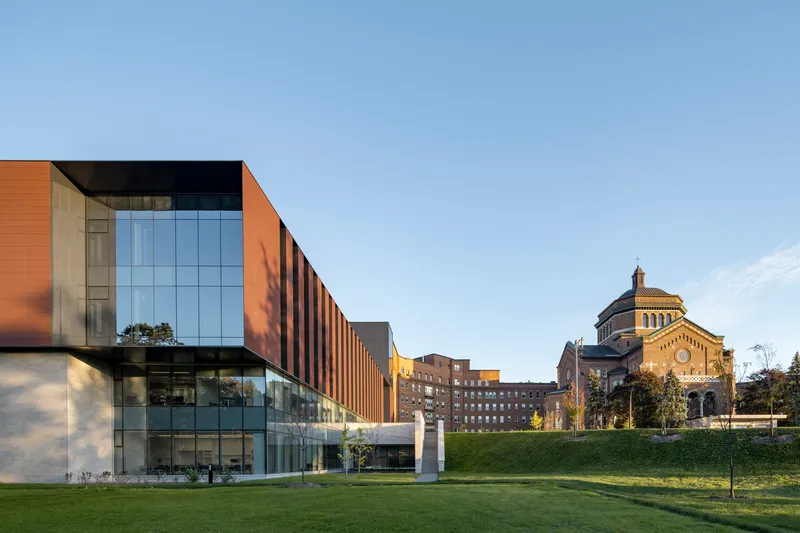 Glass and copper-toned panel facade viewed across a sloping lawn with a domed building in the background