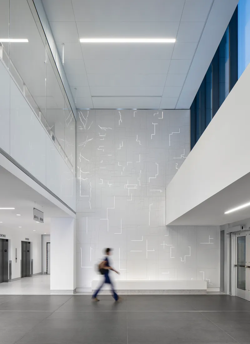 Double-height lobby with white tile wall featuring geometric relief pattern and a blurred figure walking