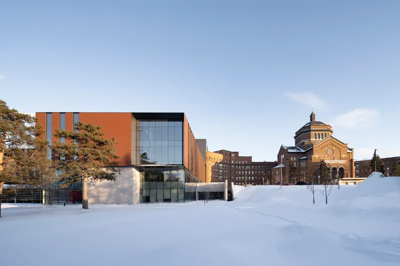 East facade of the copper-clad and glass volume across a snow-covered plaza in winter
