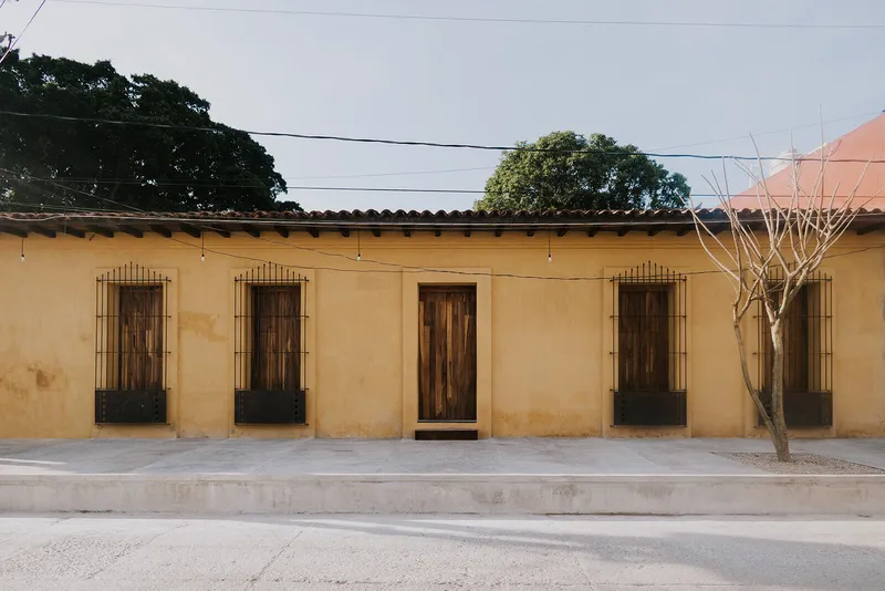 Street facade with four timber doors set in yellow ochre stucco wall beneath clay tile roof