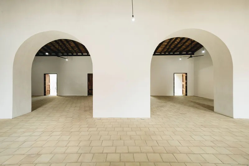 Interior room with terracotta tile floor and two arched doorways framing empty white spaces