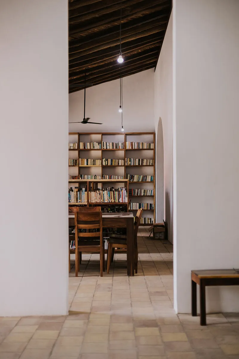 Timber dining table and chairs beside a bookshelf under an exposed rafter ceiling