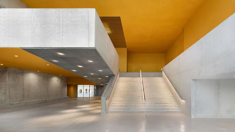 Interior lobby with concrete staircase and golden ceiling beneath a suspended acoustic panel