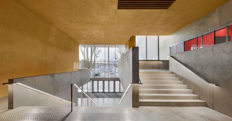 Split-level concrete staircase with golden ceiling and red-lit mezzanine windows overlooking bare winter trees