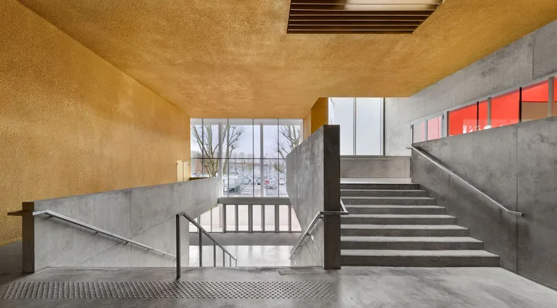 Concrete stairwell with metal railings and red accent windows under a golden vaulted ceiling