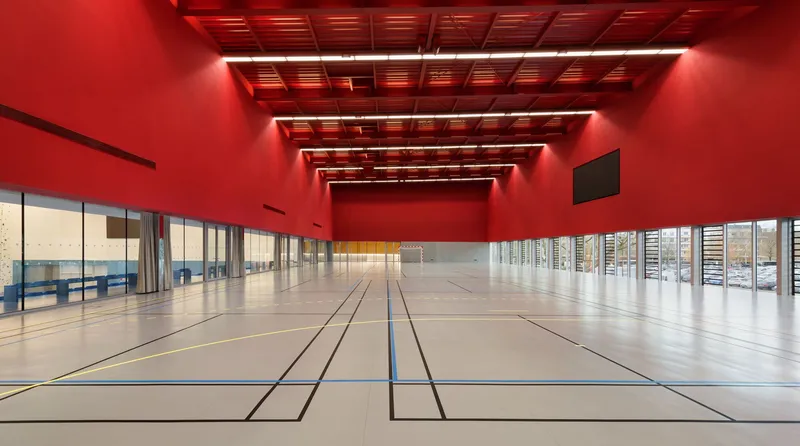 Gymnasium court with red-lit coffered ceiling and glazed wall overlooking adjacent courtyard