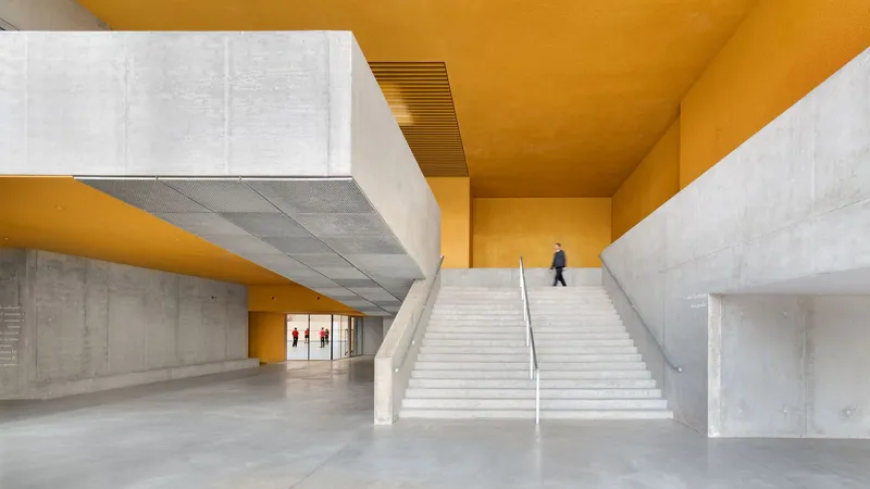 Interior lobby with wide concrete staircase and perforated metal ceiling panels beneath a yellow soffit