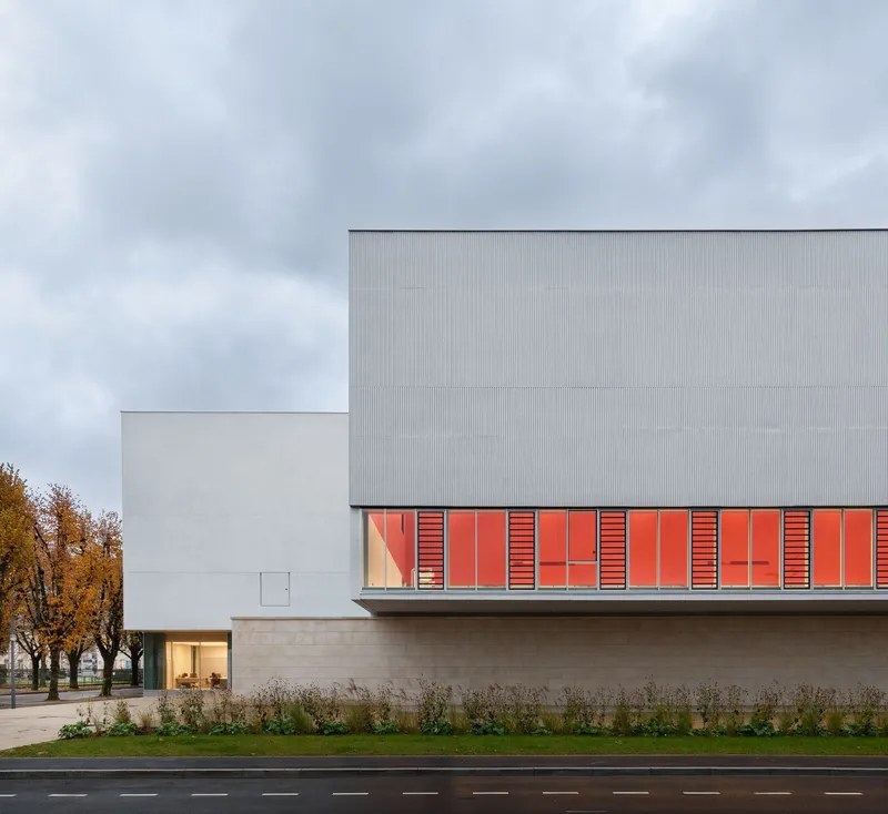 Street view of the corrugated metal facade with red louvered panels and autumn trees in the background