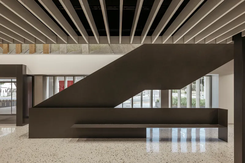 Interior lobby with dark steel staircase, terrazzo floor, and exposed timber ceiling joists