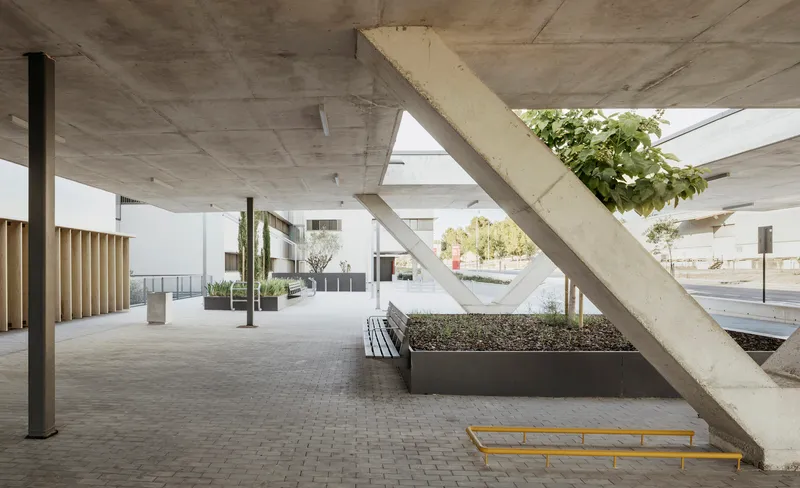 Covered porch with diagonal concrete columns, planted beds, benches, and board-formed concrete ceiling