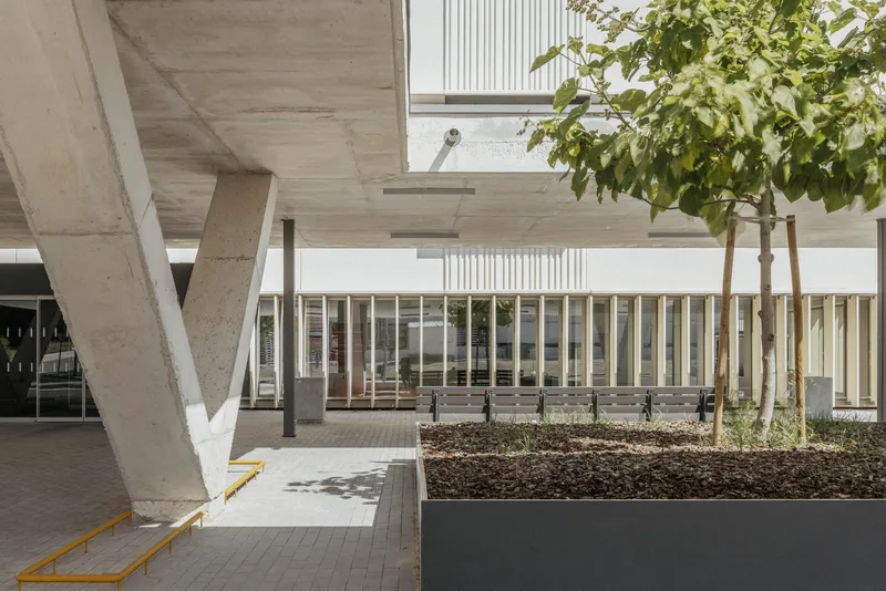 Concrete piloti supporting flat slab roof with planted raised beds and metal screen facade beyond