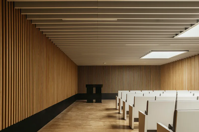 Interior assembly hall with vertical timber slat walls and ceiling and rows of white seating