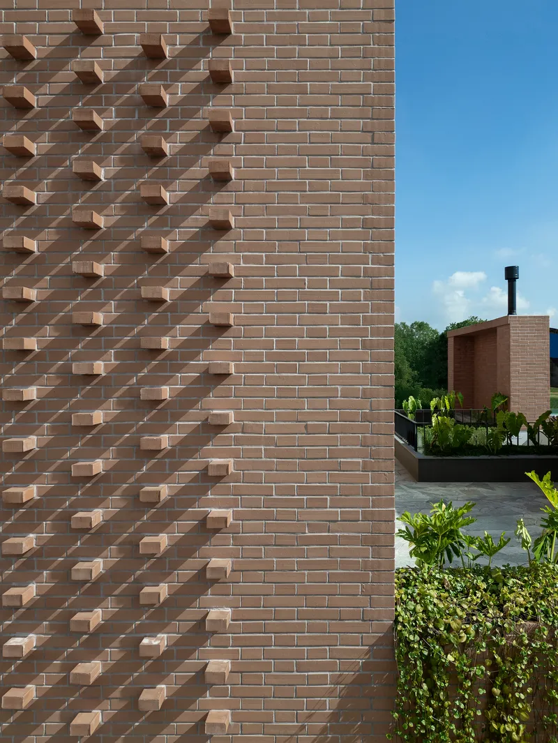 Diagonal pattern of protruding brick elements on a facade with planted courtyard visible beyond